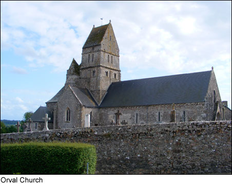 A photograph of a church set behind a stone wall and hedge.