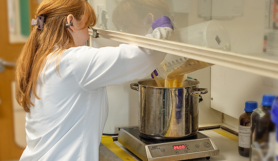 A technician wearing a lab coat, pouring media into a pan in a fume hood