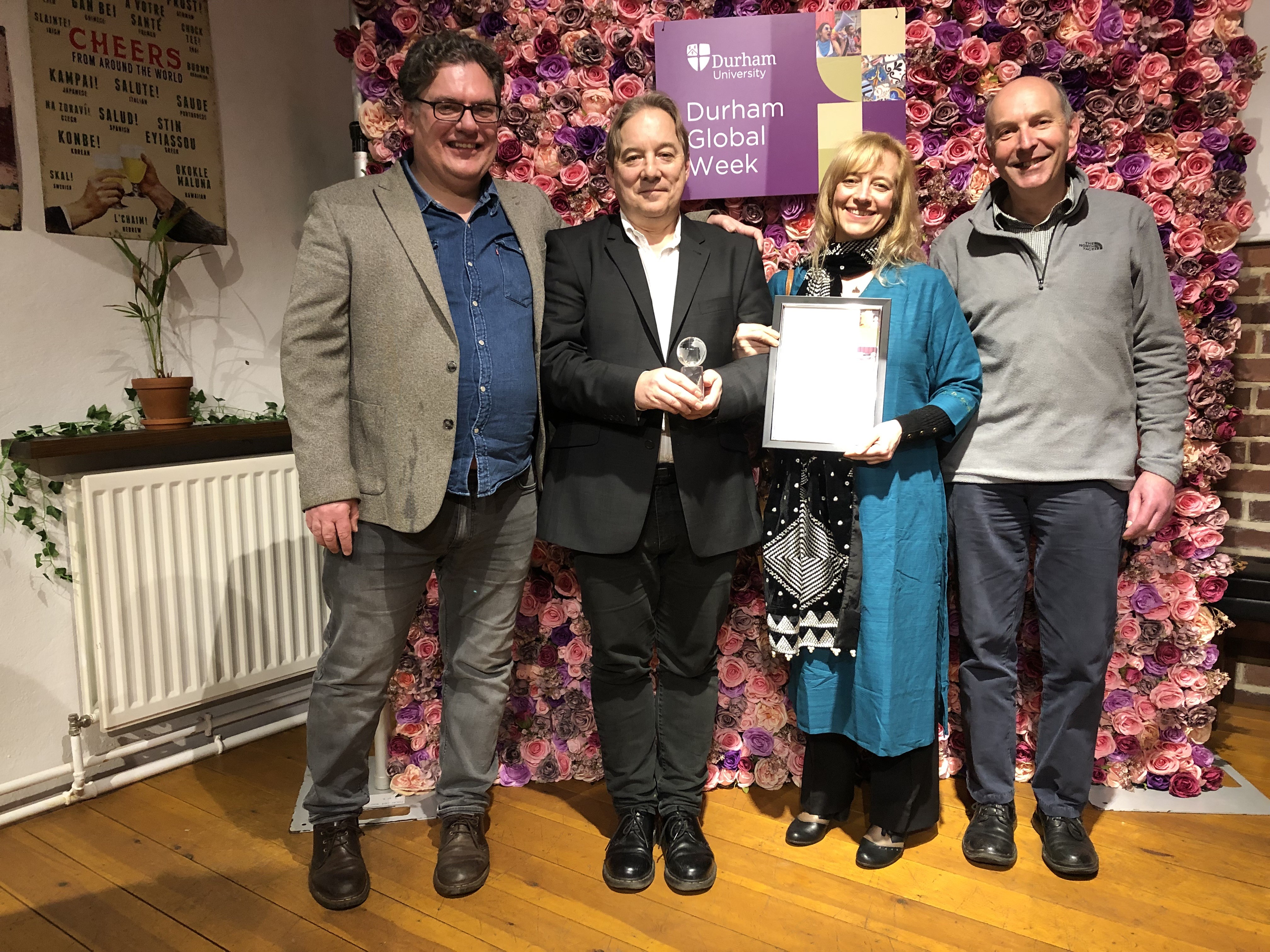 The image shows four scientist holding an award certificate