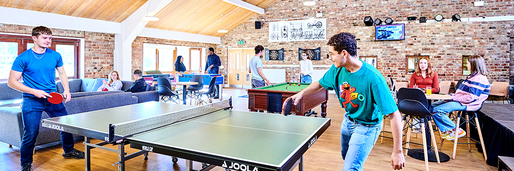 Two students play table tennis in Stephenson College Bar, other students sit a tables chatting