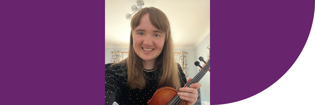 Female student with brown hair, smiling, holding violin.