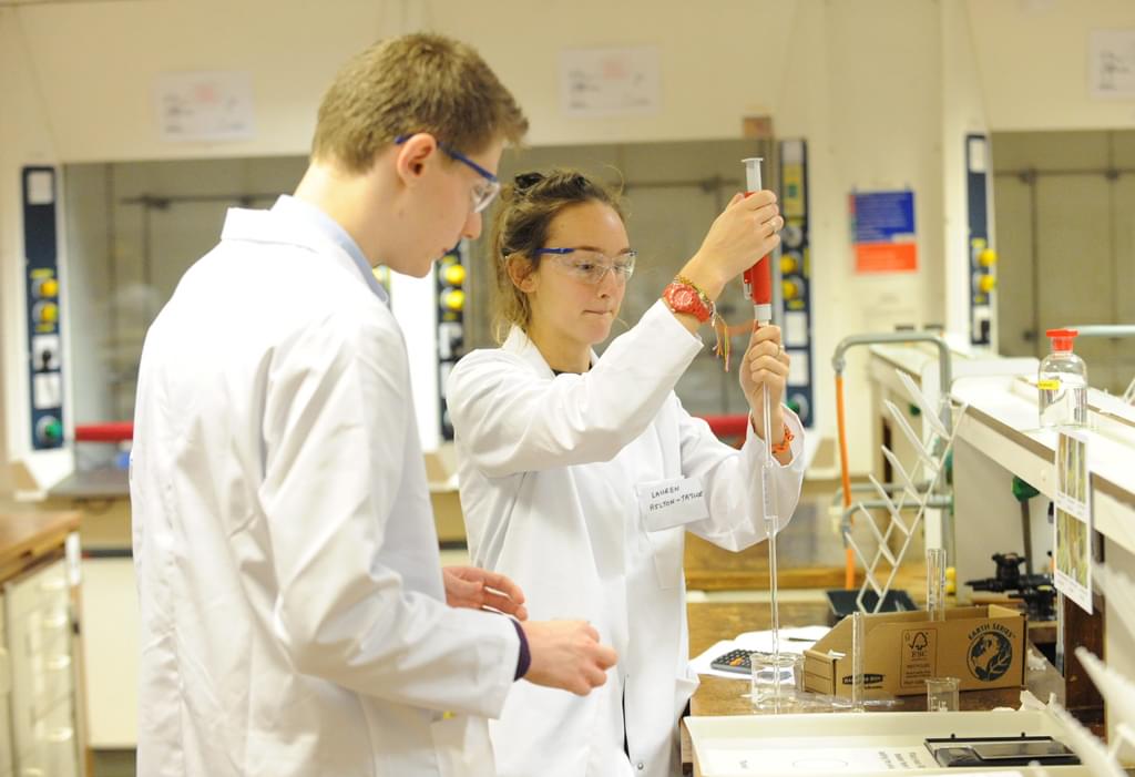 Two students in lab robes performing an experiment