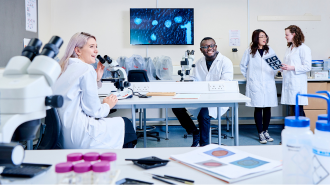 Four smiling students in a lab wearing white lab coats.