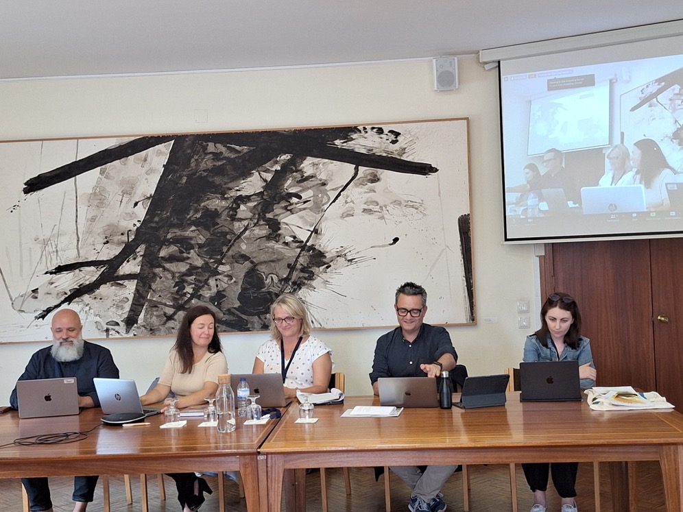 Five people working on laptops with abstract artwork and a screen behind them