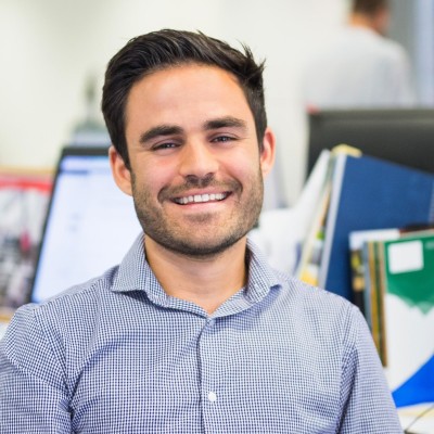 A male academic with dark hair smiling, wearing a blue checked shirt.