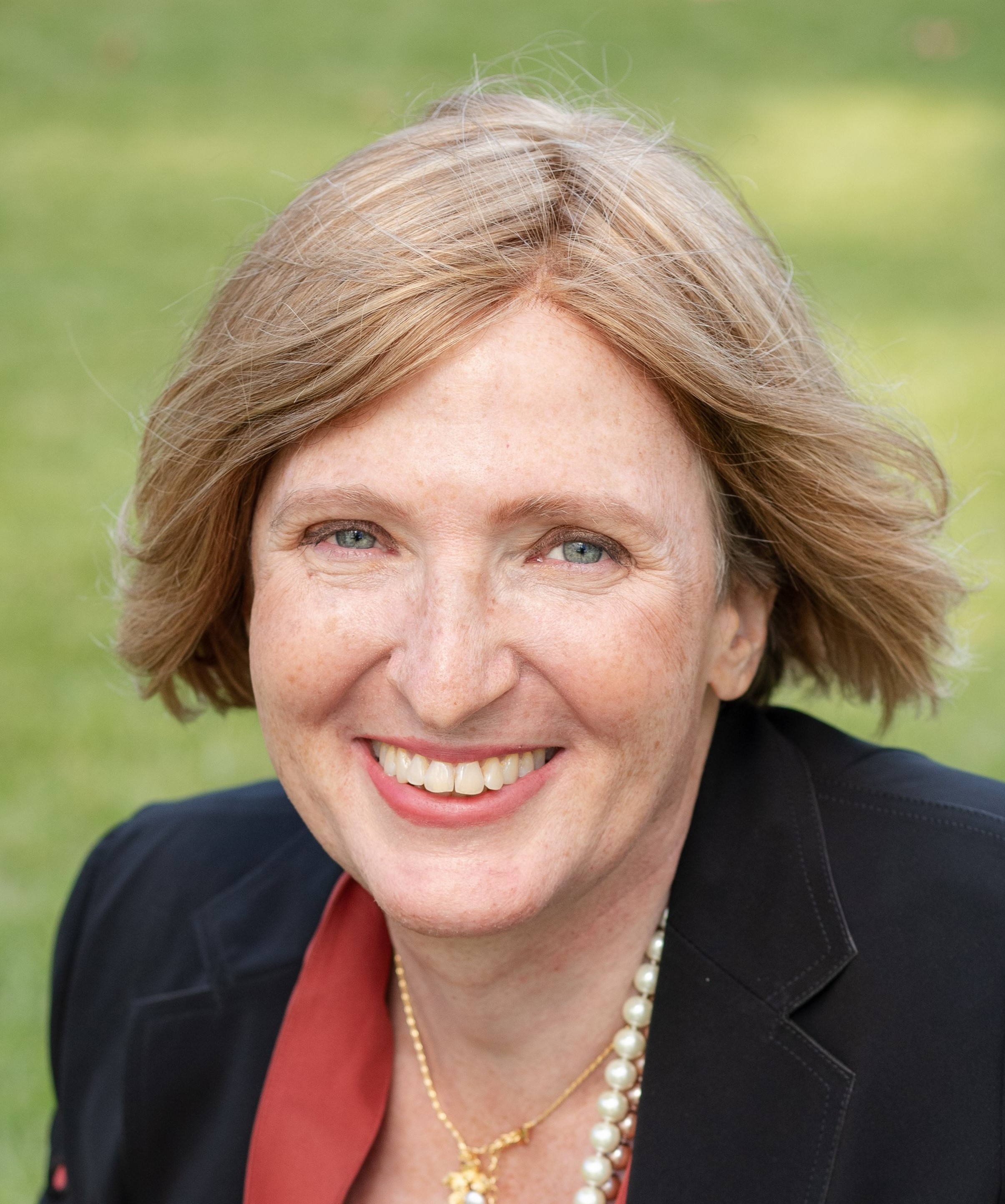 Smiling woman with black blazer and pearl necklace
