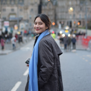 Female student smiling over her shoulder wearing a black coat and blue scarf