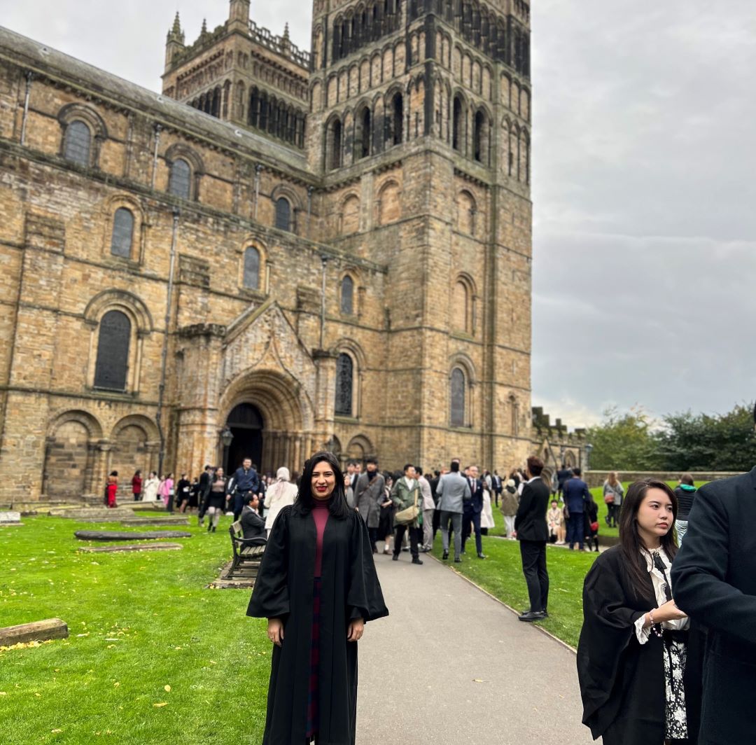 Student looking at the camera with graduation gown on, in front of cathedral