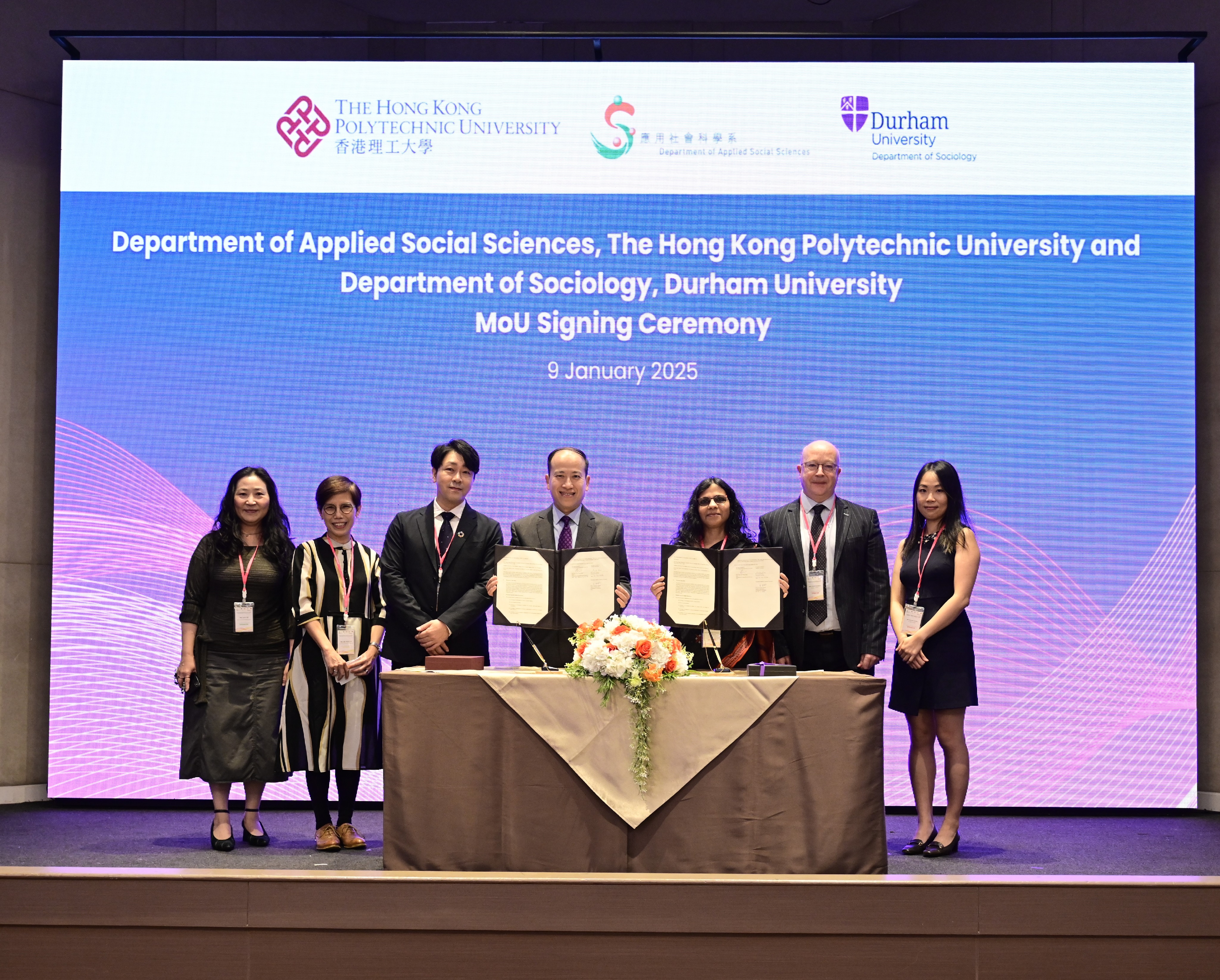 Colleagues facing camera standing on a stage, holding signed agreements