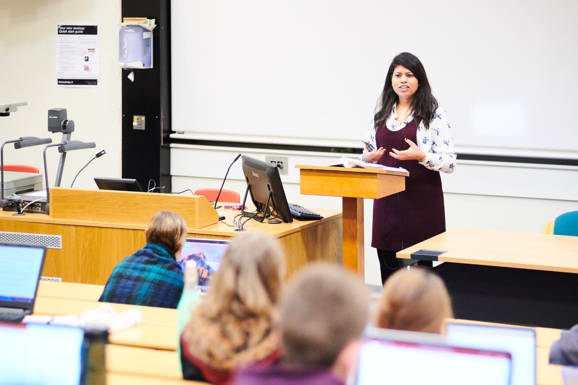 Someone at a lectern giving a lecture to a group of students