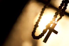 A rosary with a cross hanging with light in the background.