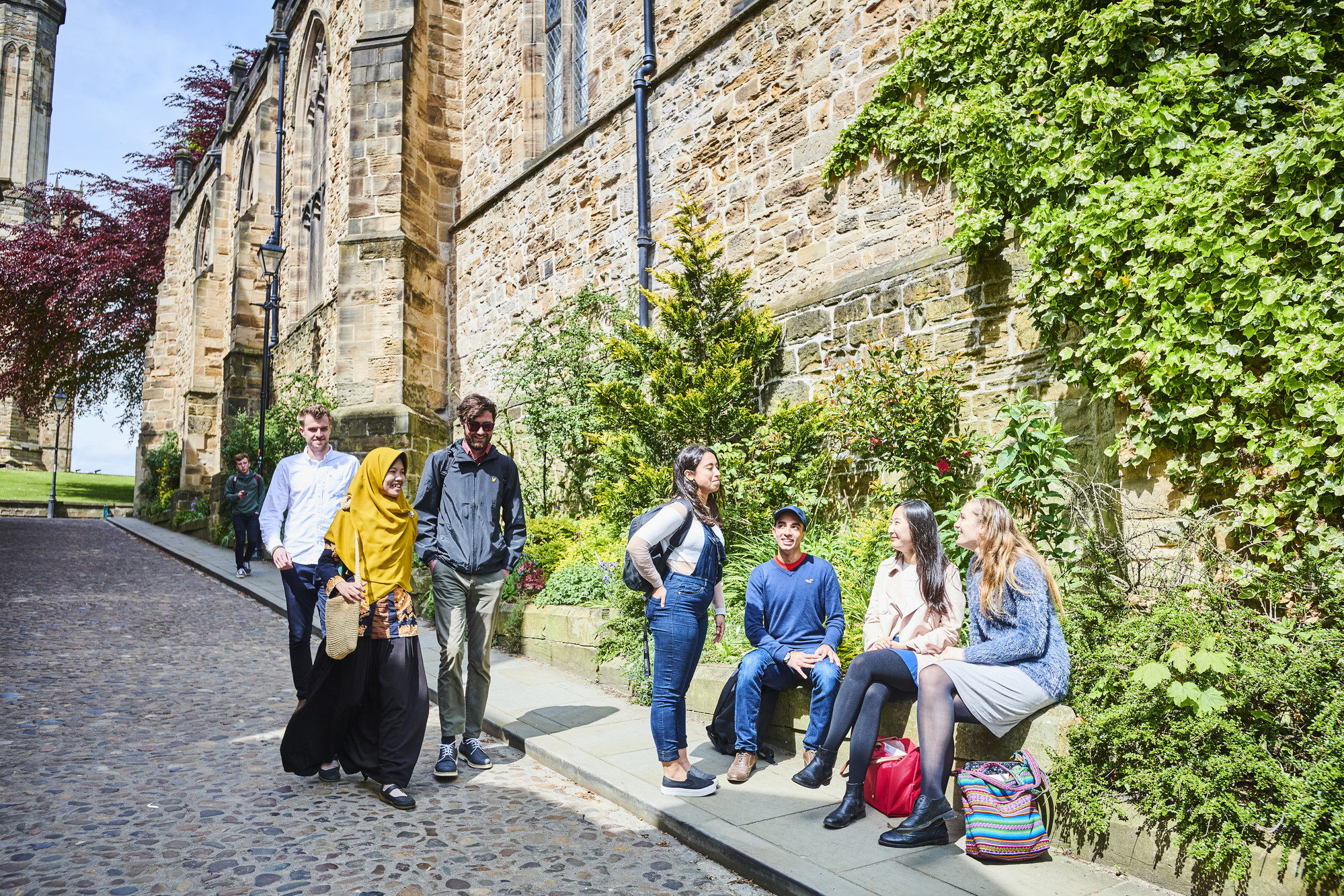 Students walking down Bow Lane by group sitting on wall