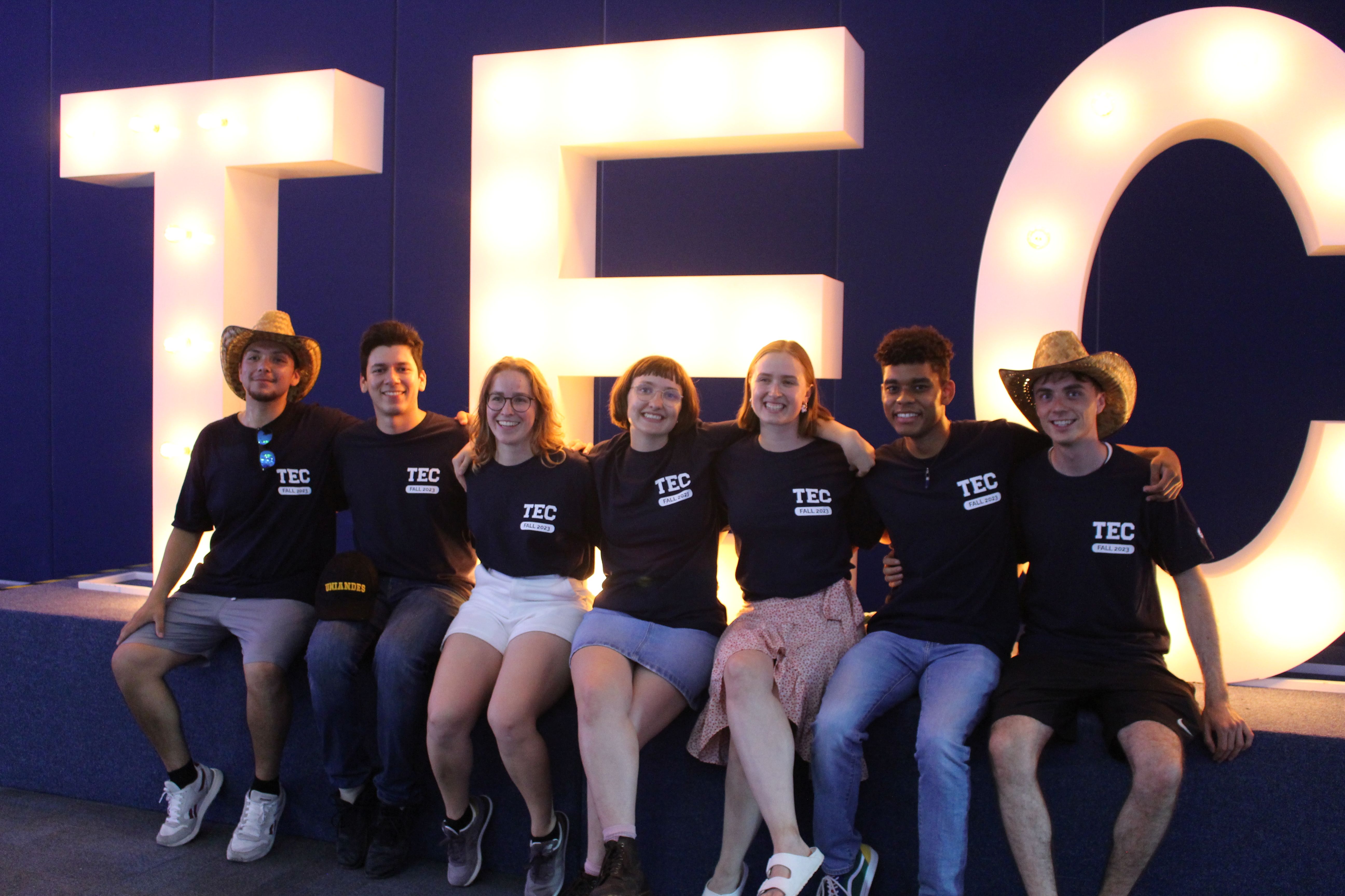 Group of students sitting in front of a large lit up logo of Tec De Monterrey University