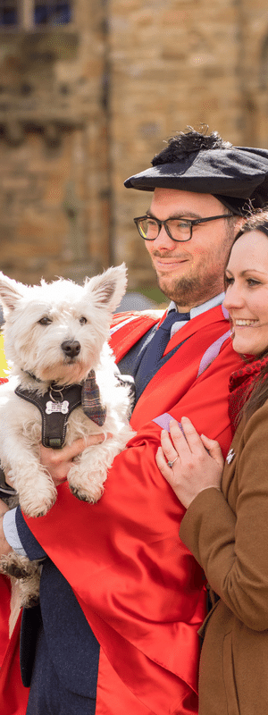 Student graduates in gowns with a dog