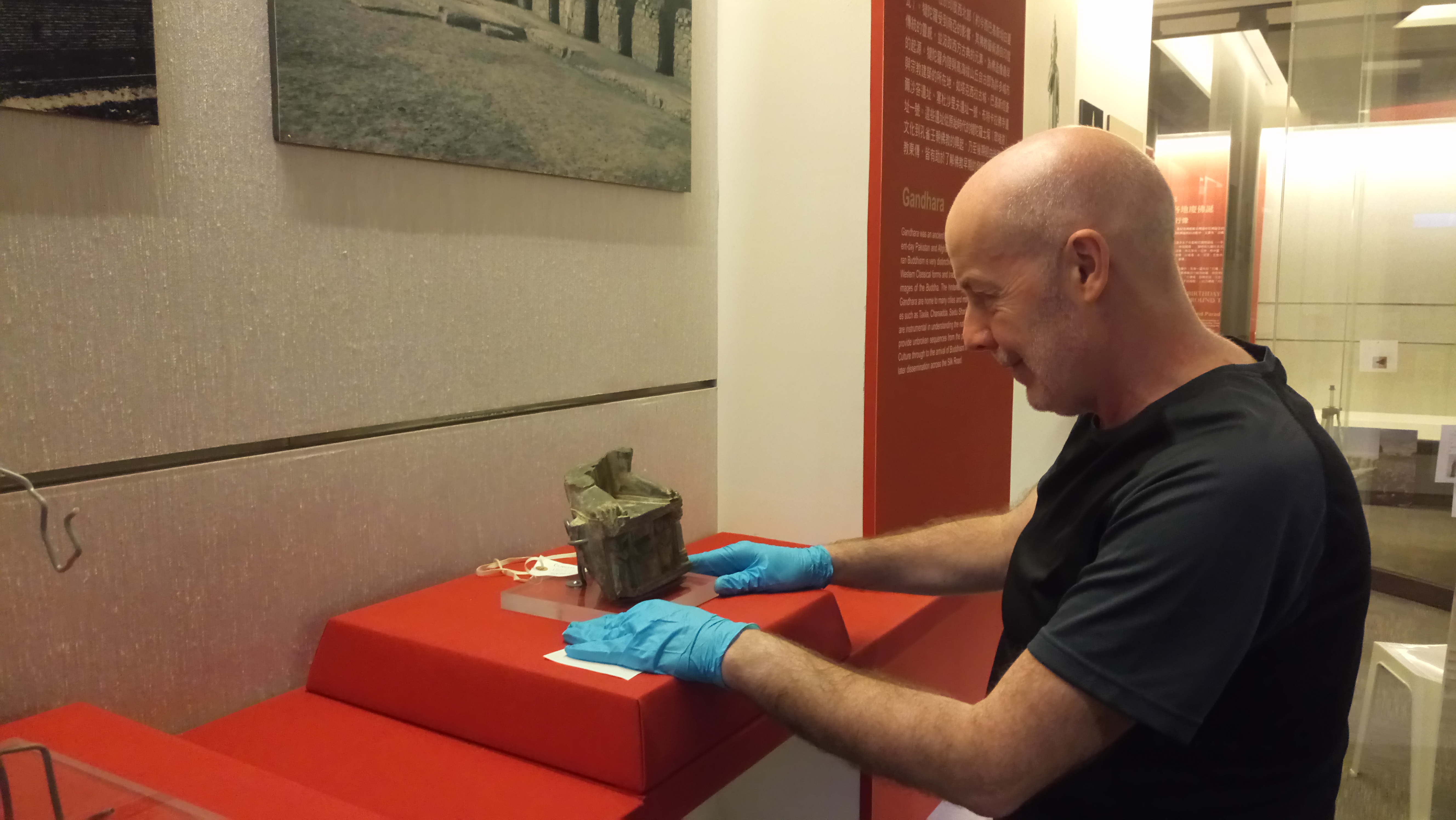 A man wearing purple gloves positions a stone sculpture into a museum display case