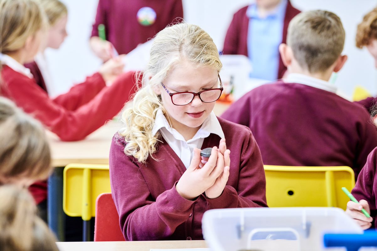 A child dressed in school uniform sits at a table studying an ancient Egyptian scarab