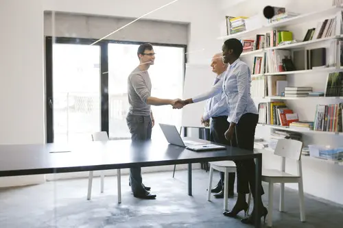 Two people shaking hands in an interview at a desk in an office