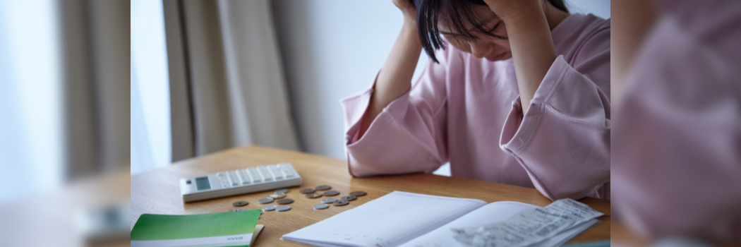 A person with head in their hands looking a bank statements and money on the table