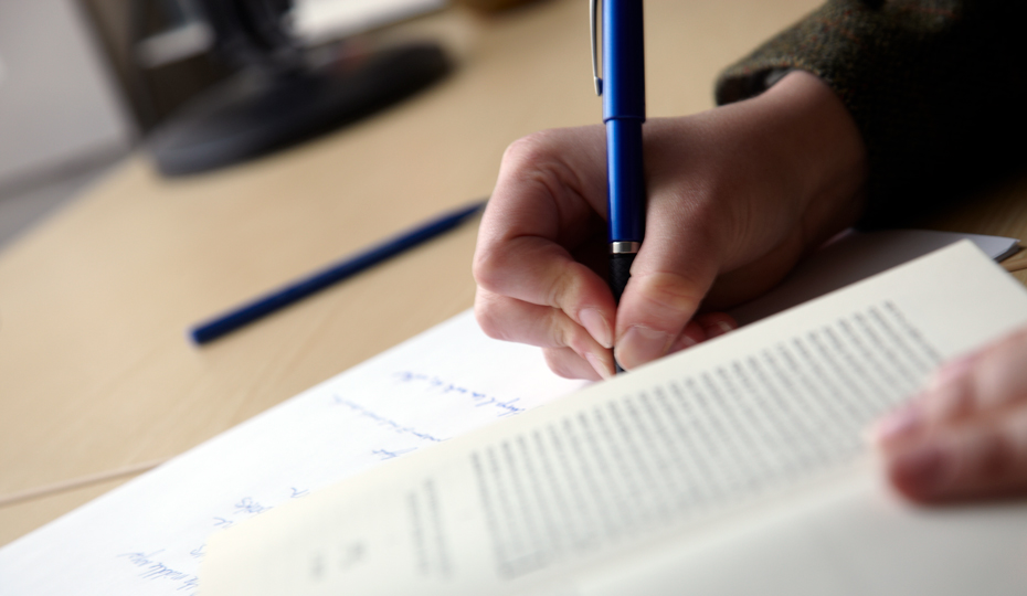 A person making notes from a textbook