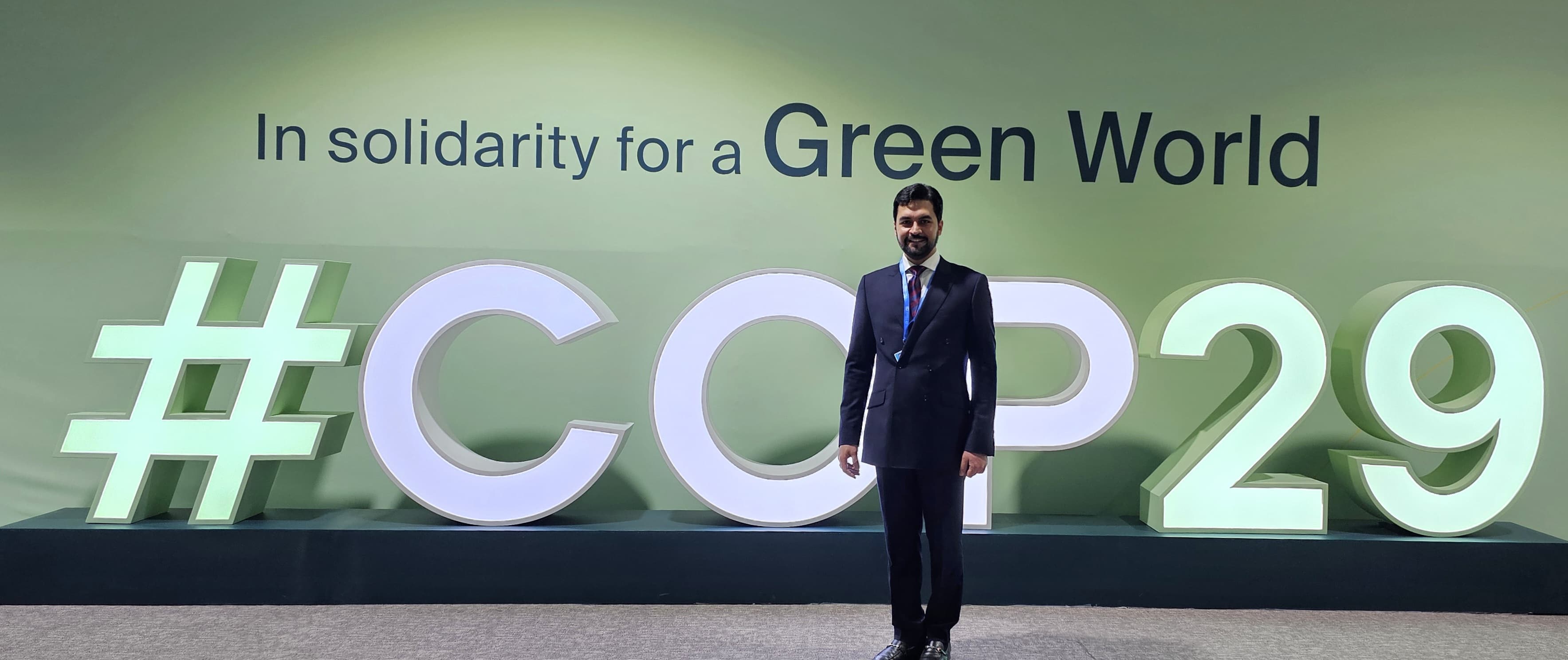 a man in suit standing in front of COP29 hashtag sign