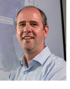 A man standing in front of a world map smiling