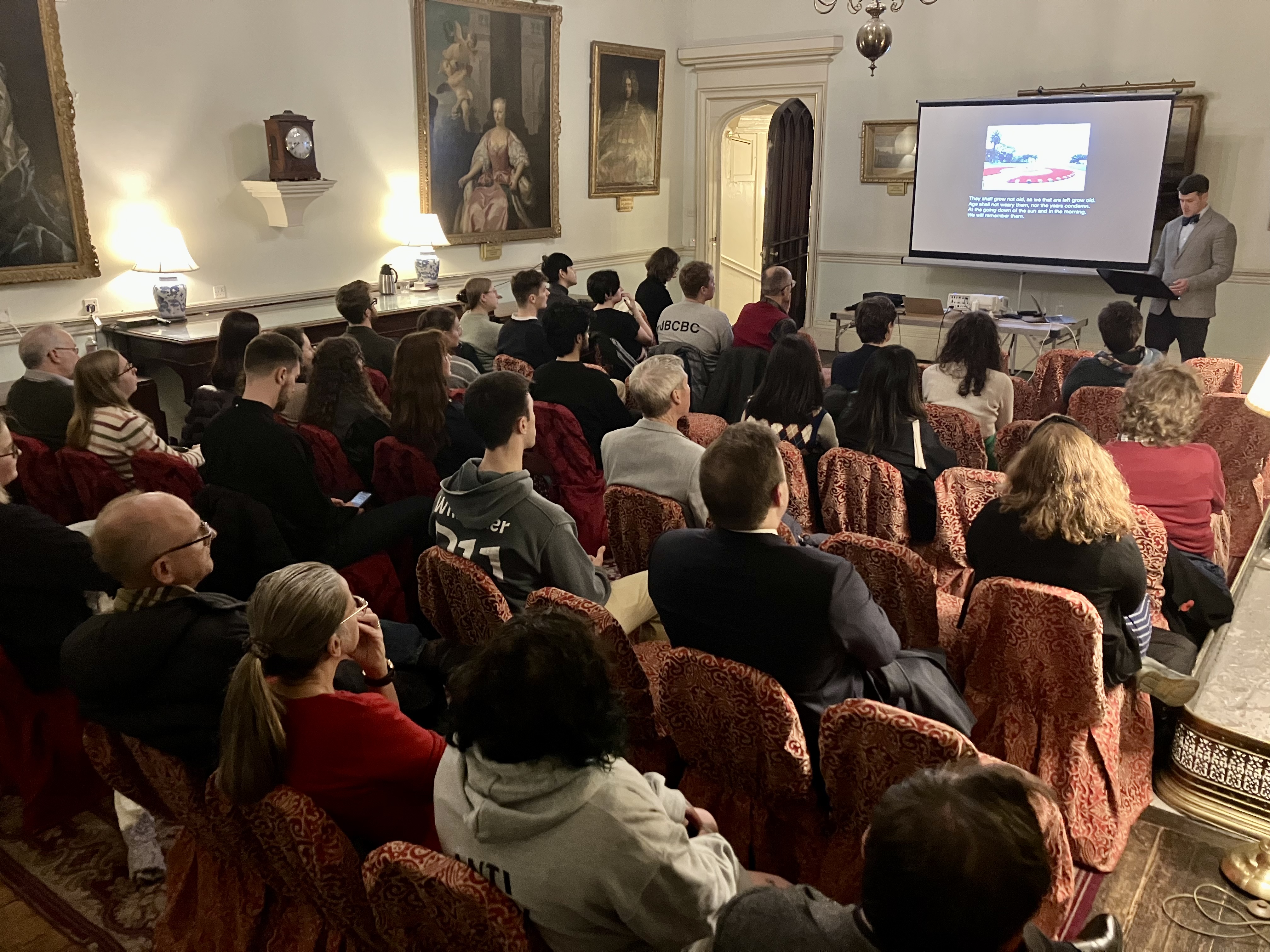 Around 35 people sitting in a grand room looking at a man giving a lecture