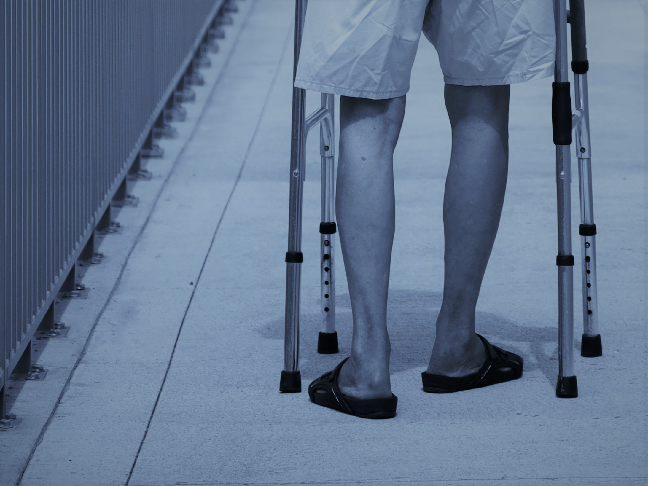 Black and white photo with blue filter of man's legs with zimmer frame