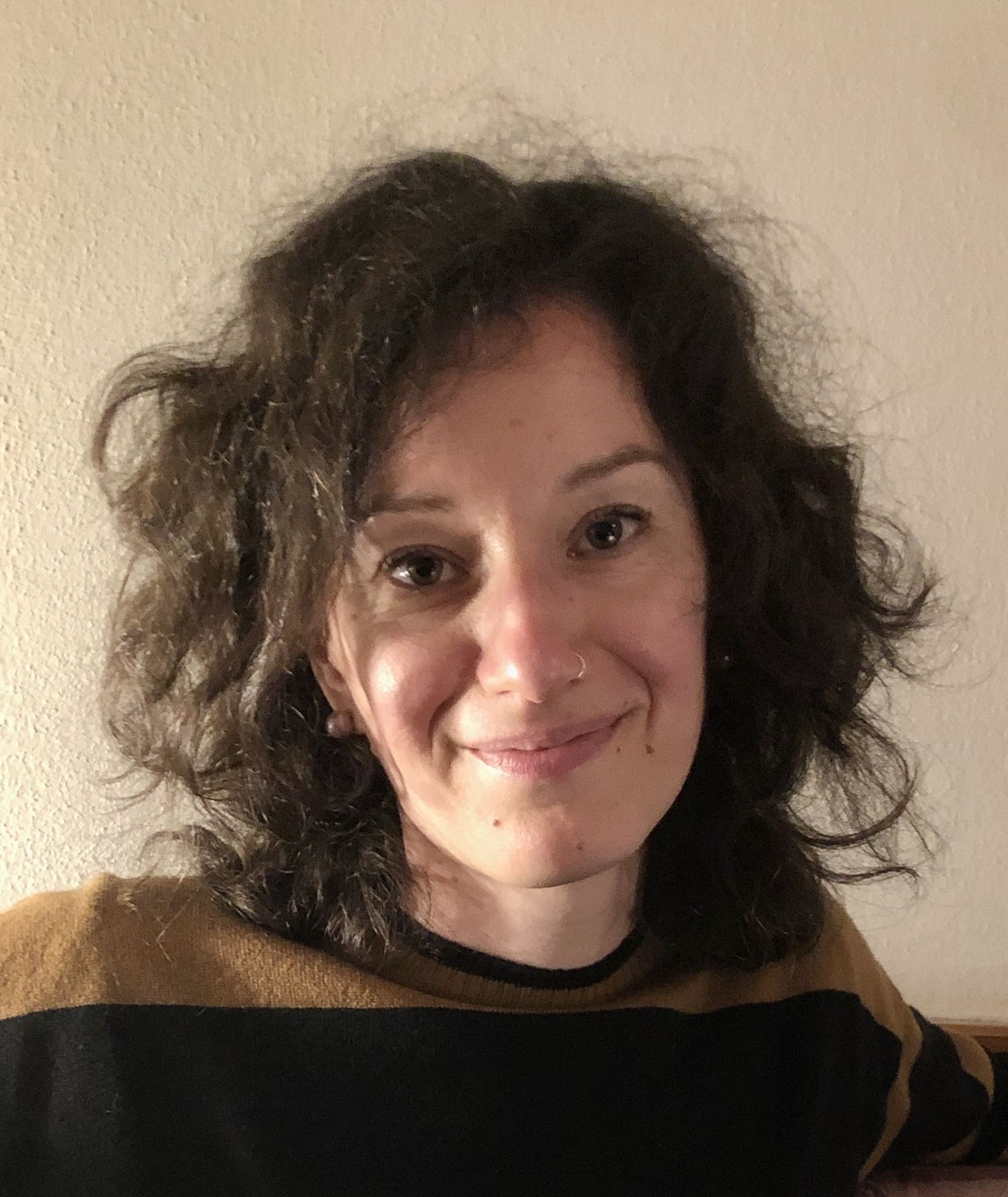 Portrait of white female with striped, brown jumper, curly brown hair and a nose ring