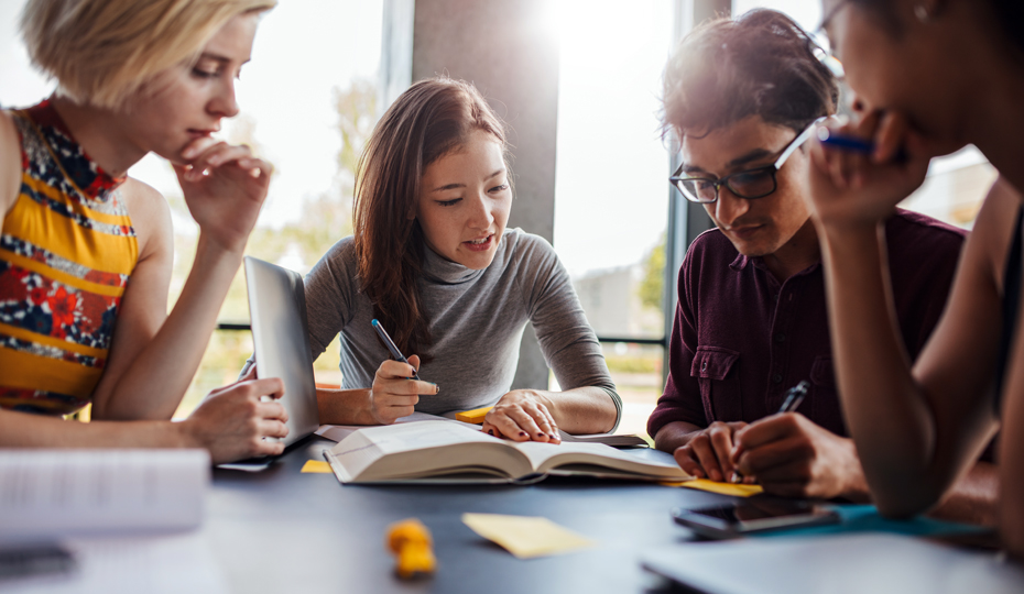 A group of students sitting around a table studying and discussing open books