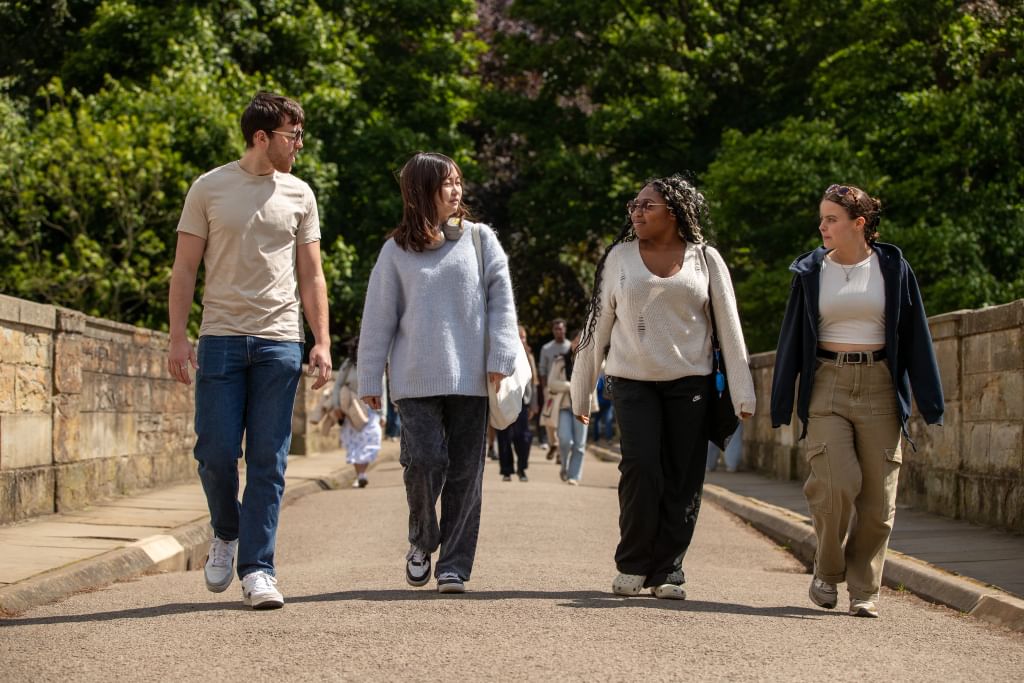 Four students walking across a bridge in the sunshine