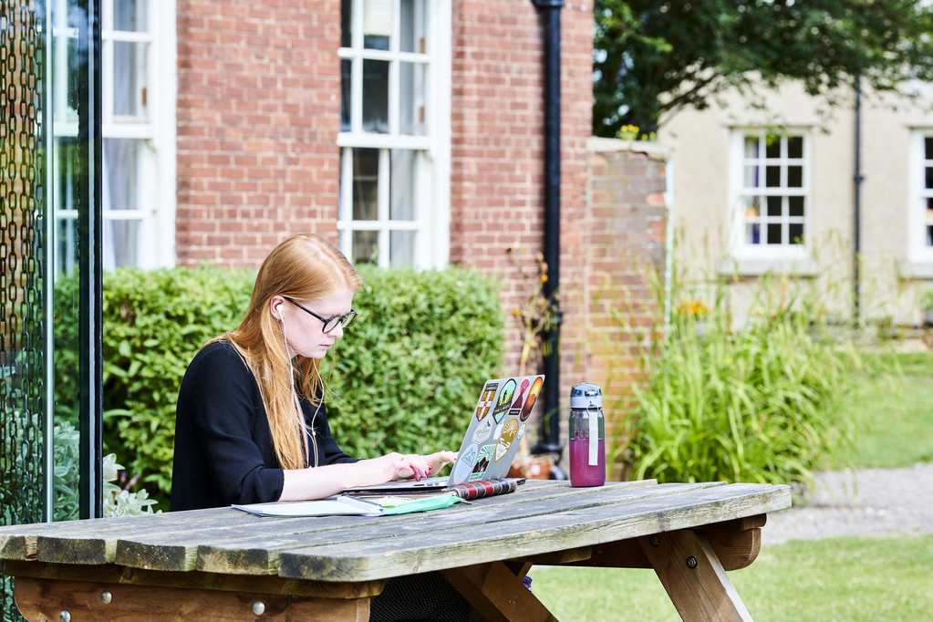 A student sitting outside, working on her laptop.