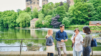 Four students by the riverside with cathedral in the background