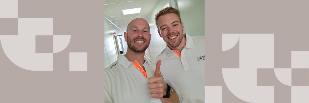 Two men wearing white polo shirts standing together grinning at the camera making a thumbs up sign