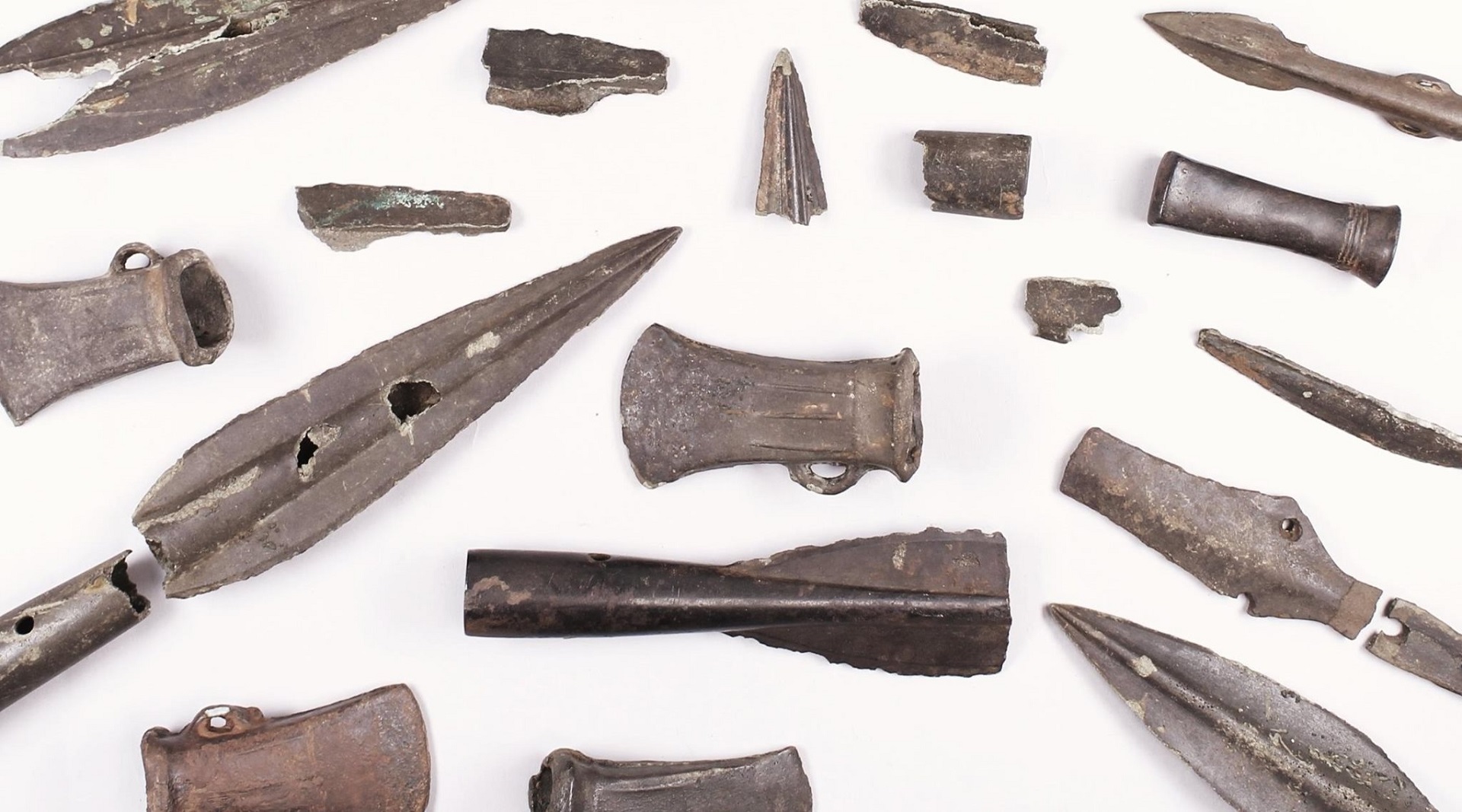 A coloured photograph showing several broken and complete bronze age swords and axes.