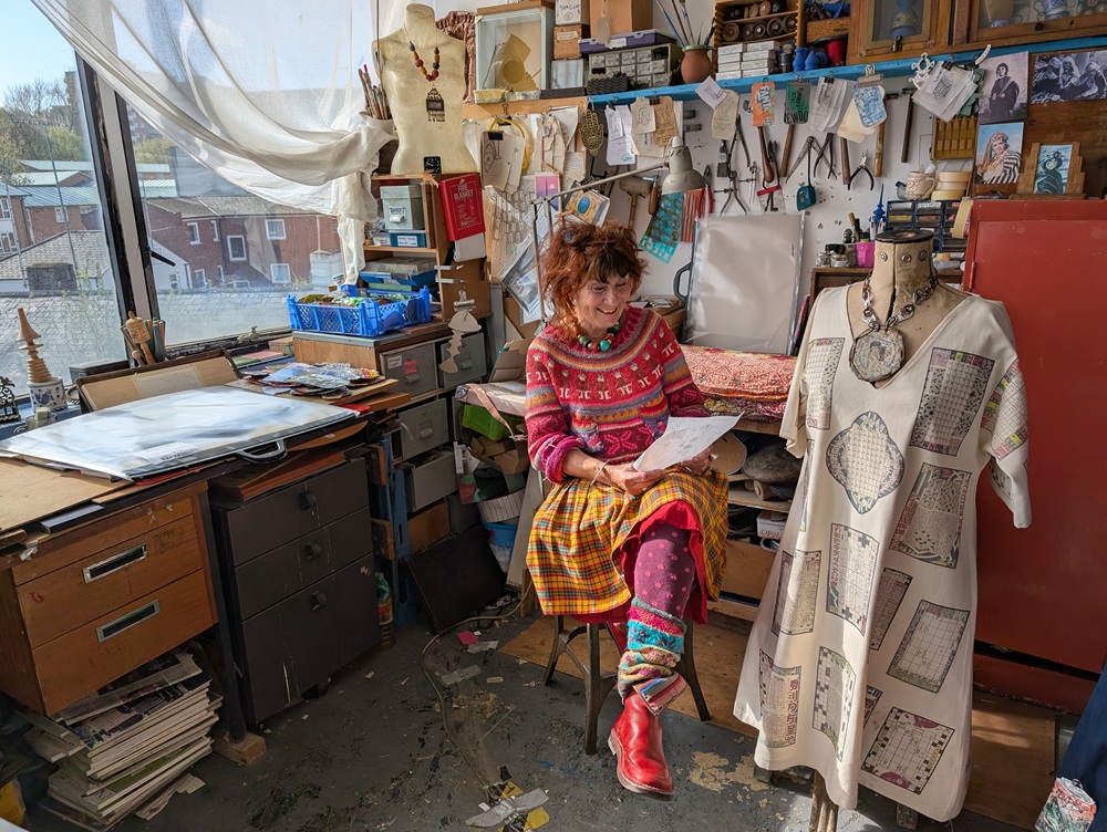 A woman sits on a chair in an artist studio surrounded by artworks